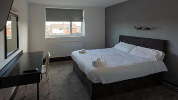 A bedroom with a bed, a desk, a chair, a window, and a radiator.