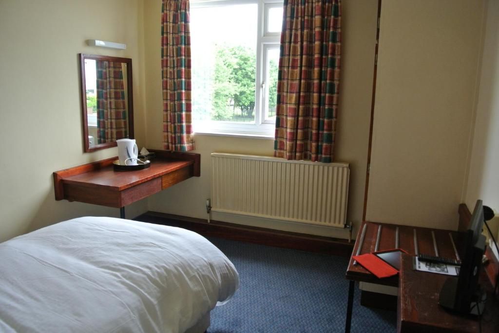 Une chambre d’hôtel avec un lit, un bureau avec un ordinateur, une fenêtre avec des rideaux et un radiateur.