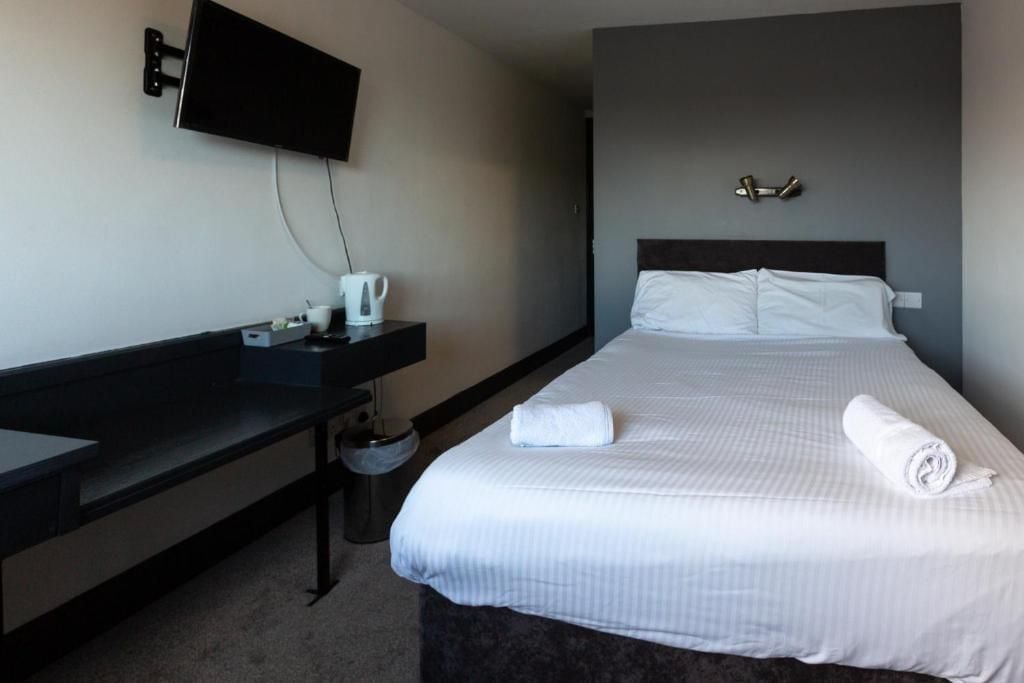 A hotel room with a bed, a bedside table, a TV mounted on the wall, and a trash bin.