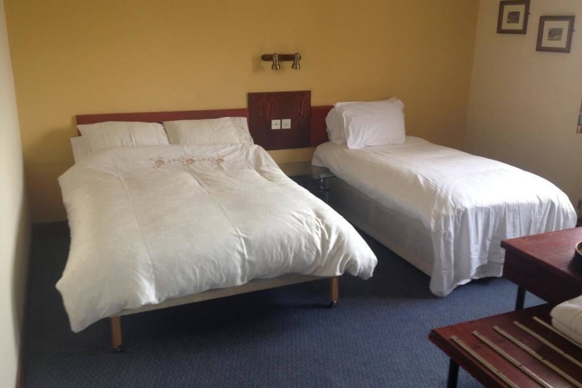 A hotel room with two single beds, a wooden headboard, a small wooden table, and a bench.