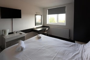 Una habitación de hotel con cama, escritorio, silla, televisor y ventana.