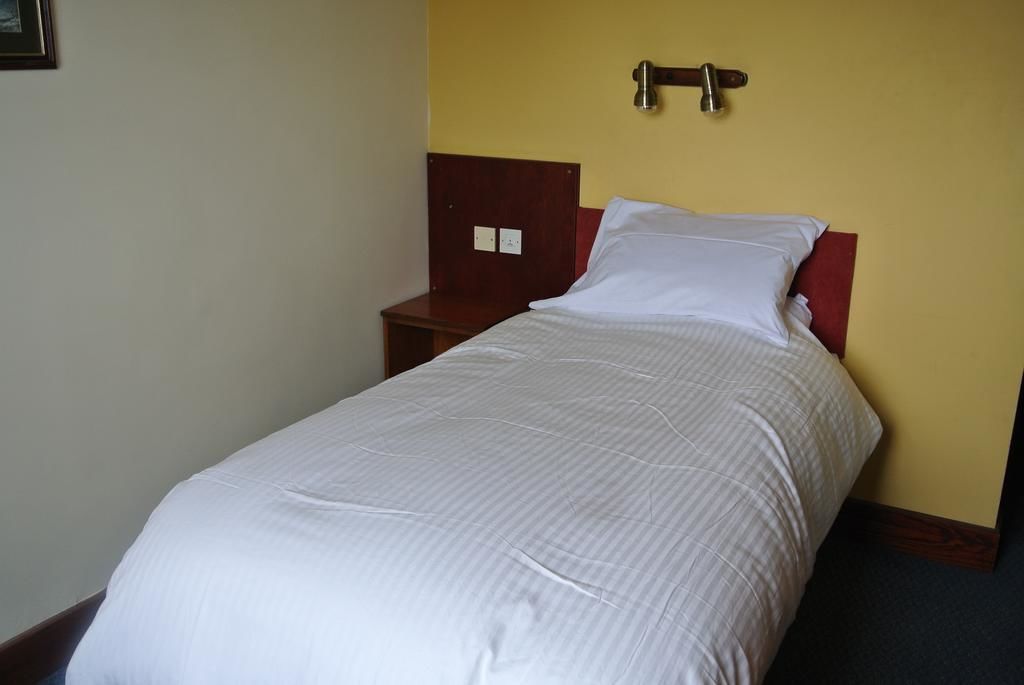 A single bed with a wooden headboard and a red accent, a nightstand, and a wall-mounted light fixture.
