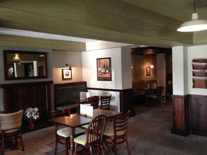A restaurant interior with wooden tables and chairs, framed pictures on the walls, and a hanging light fixture.