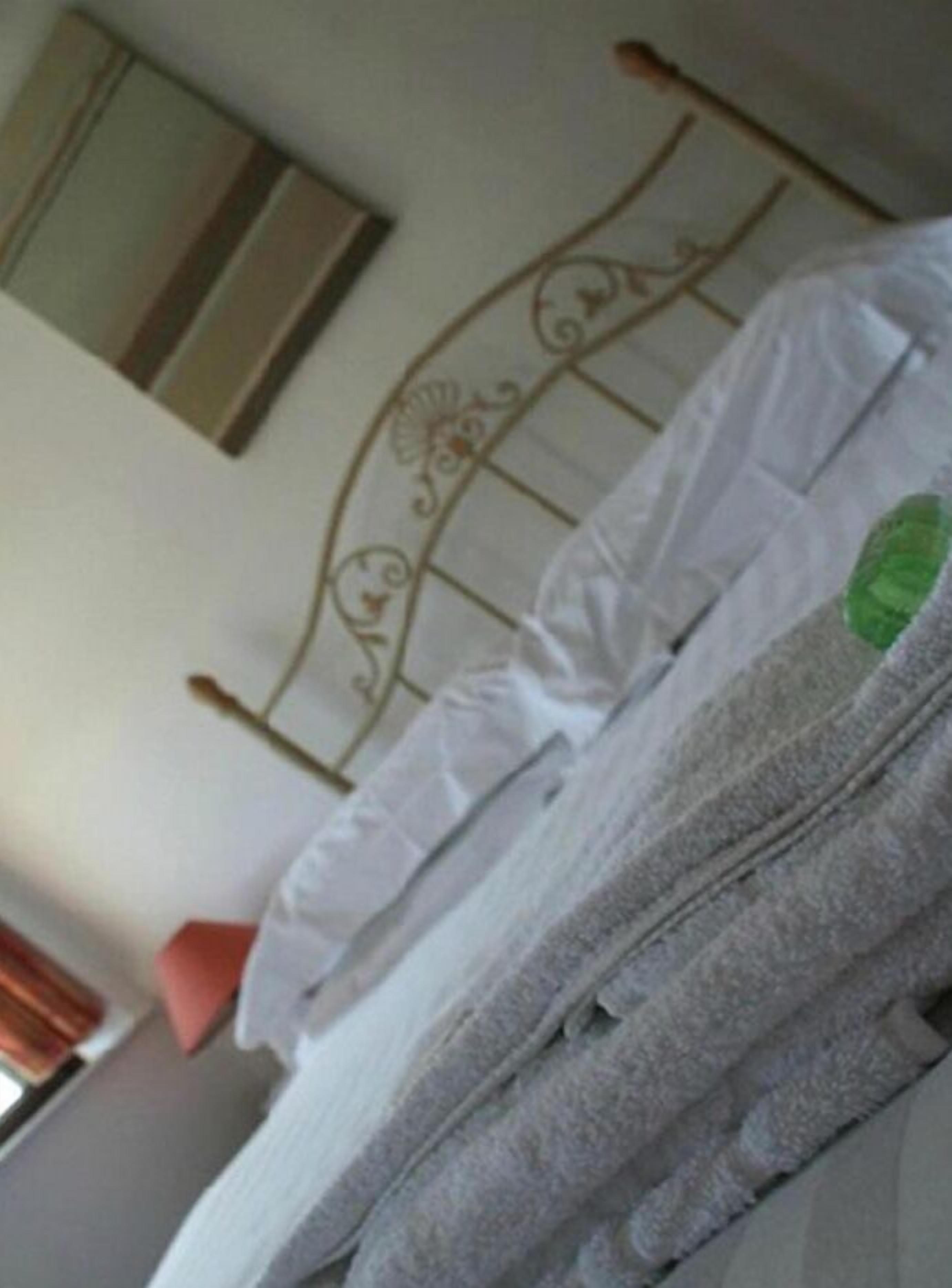 Cama arrumada com roupa de cama branca e manta cinza.