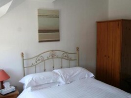 Un dormitorio con estructura de cama metálica, ropa de cama blanca, un armario de madera y una mesita de noche con una lámpara y un teléfono.