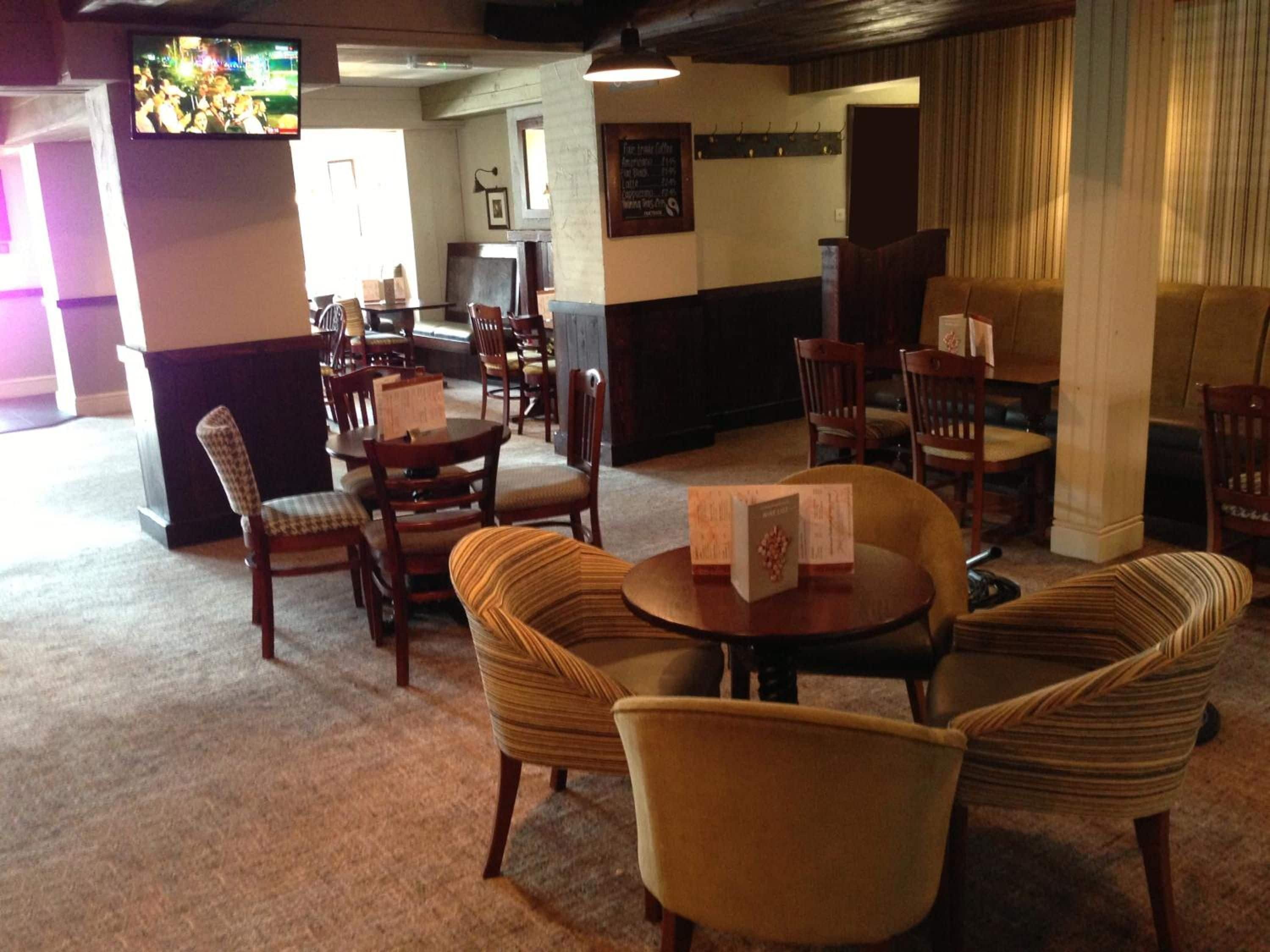 A hotel lobby with a mix of seating options including round tables and cushioned chairs, a television mounted on the wall, and a menu board displaying room rates.