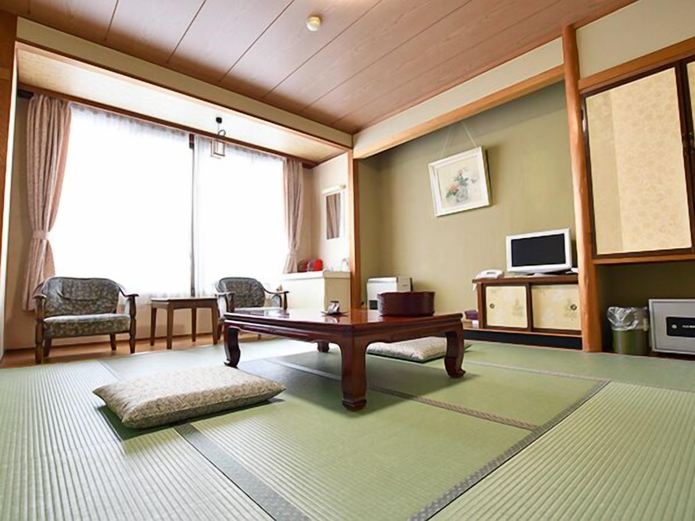 A traditional Japanese-style room with tatami flooring, a low table, two chairs, a television, and a cabinet.