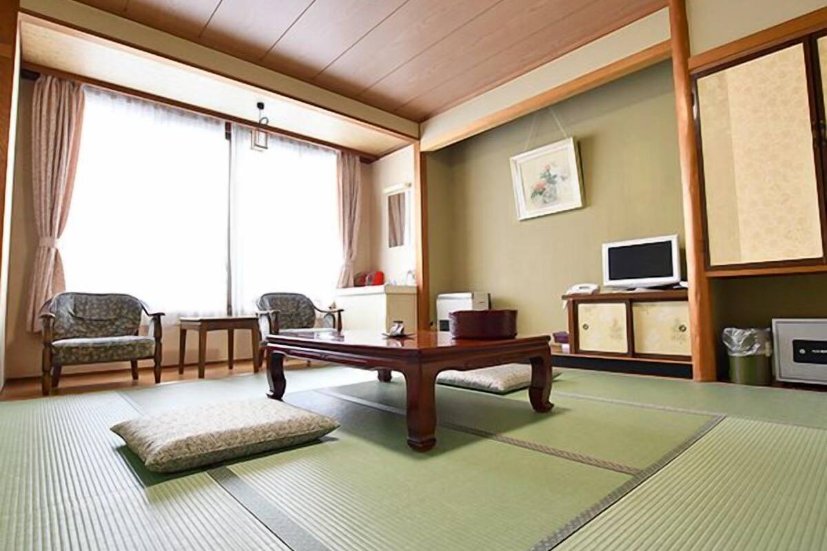 Ein traditioneller japanischer Raum mit Tatami-Böden, einem niedrigen Tisch, zwei Stühlen, einem Fernseher und einem Schrank.