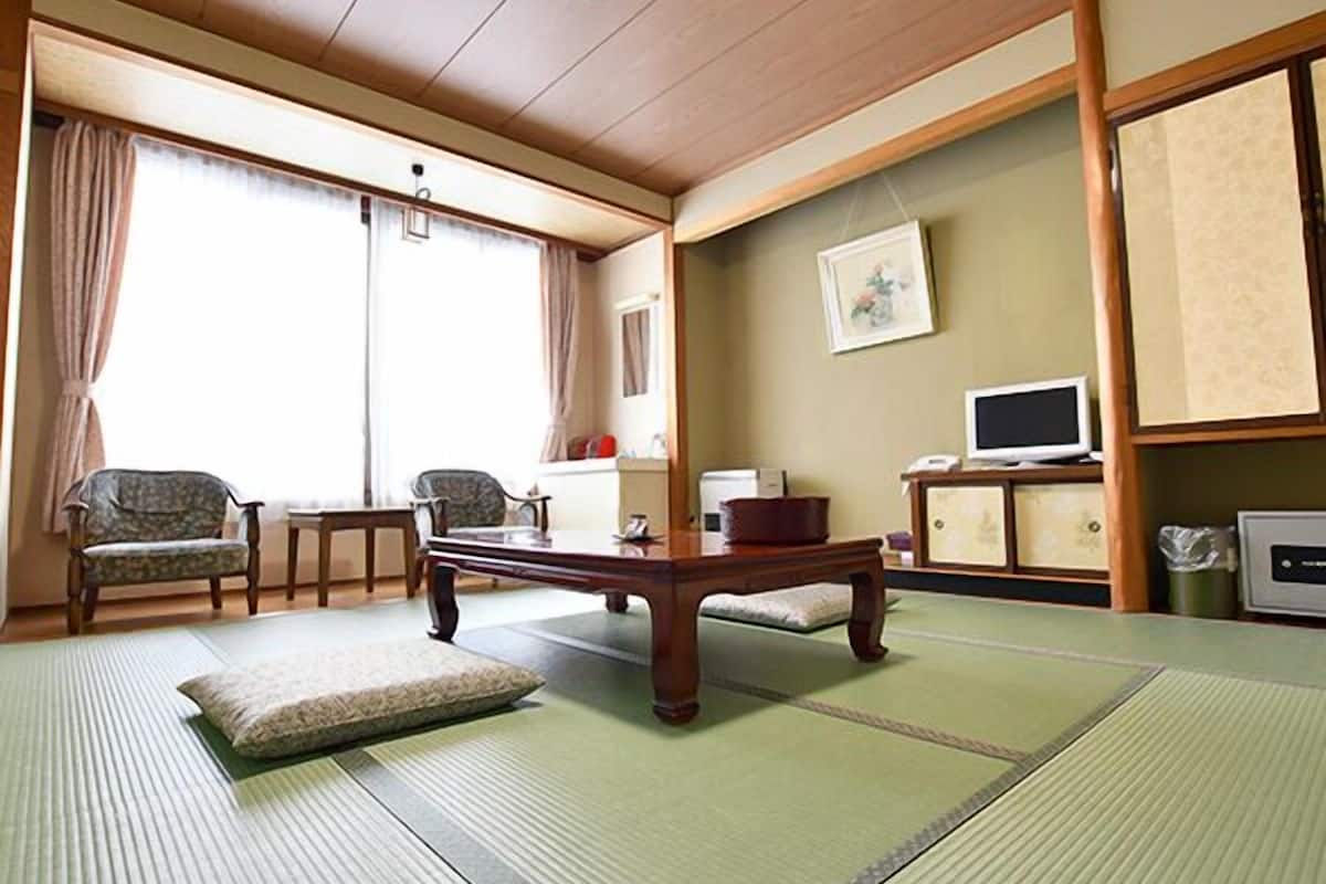 A traditional Japanese-style room with tatami flooring, a low table, two chairs, a television, and a cabinet.