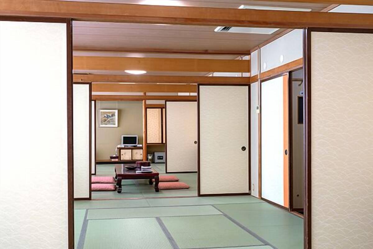Ein traditioneller japanischer Raum mit Tatami-Boden, Schiebetüren und einem niedrigen Tisch mit Kissen.