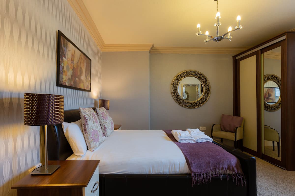 A hotel room with a bed, a bedside lamp, a mirror, and a chair.