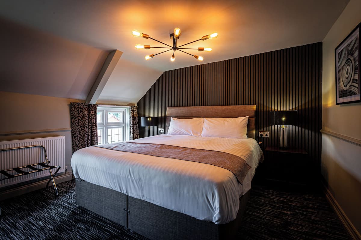 A modern hotel room with a large bed, a sloped ceiling, a wall-mounted TV, and a unique ceiling light fixture.