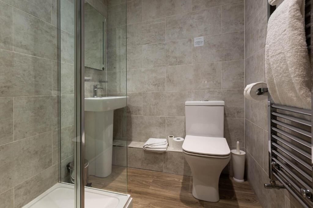 Un baño moderno con cabina de ducha de vidrio, inodoro, lavabo y toallero.