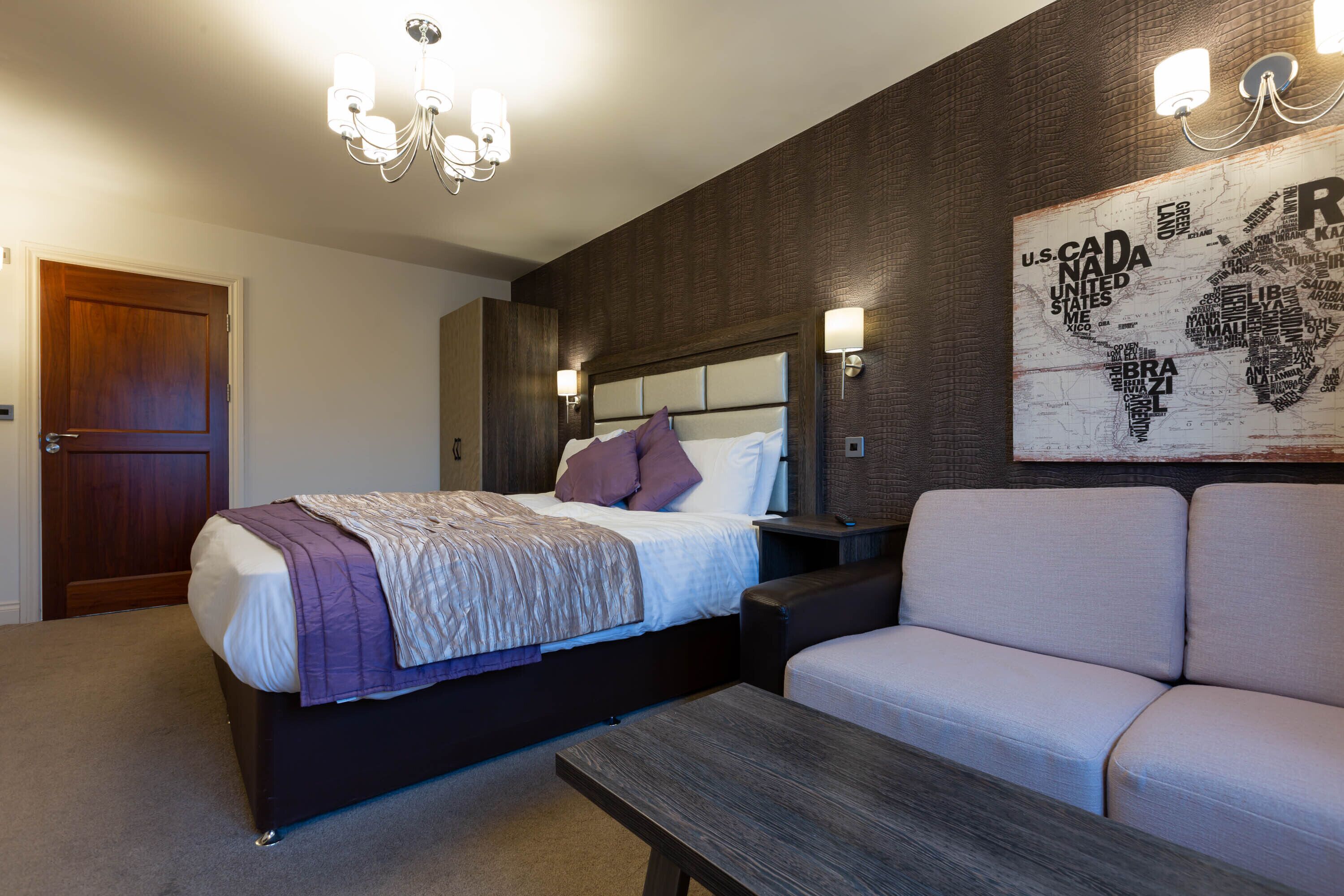 A modern bedroom with a bed, a sofa, a wooden table, and a world map mural on the wall.