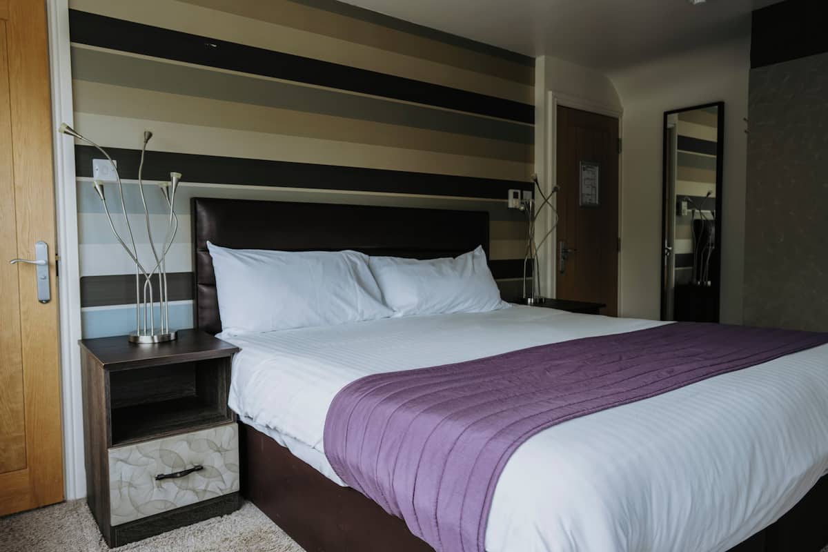A bedroom with a bed, nightstands, a drawer unit, a purple throw, and a mirror.