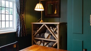 A room with a wooden table, a lamp, a mirror, and a shelf with logs. - The White Swan (Gainsborough)