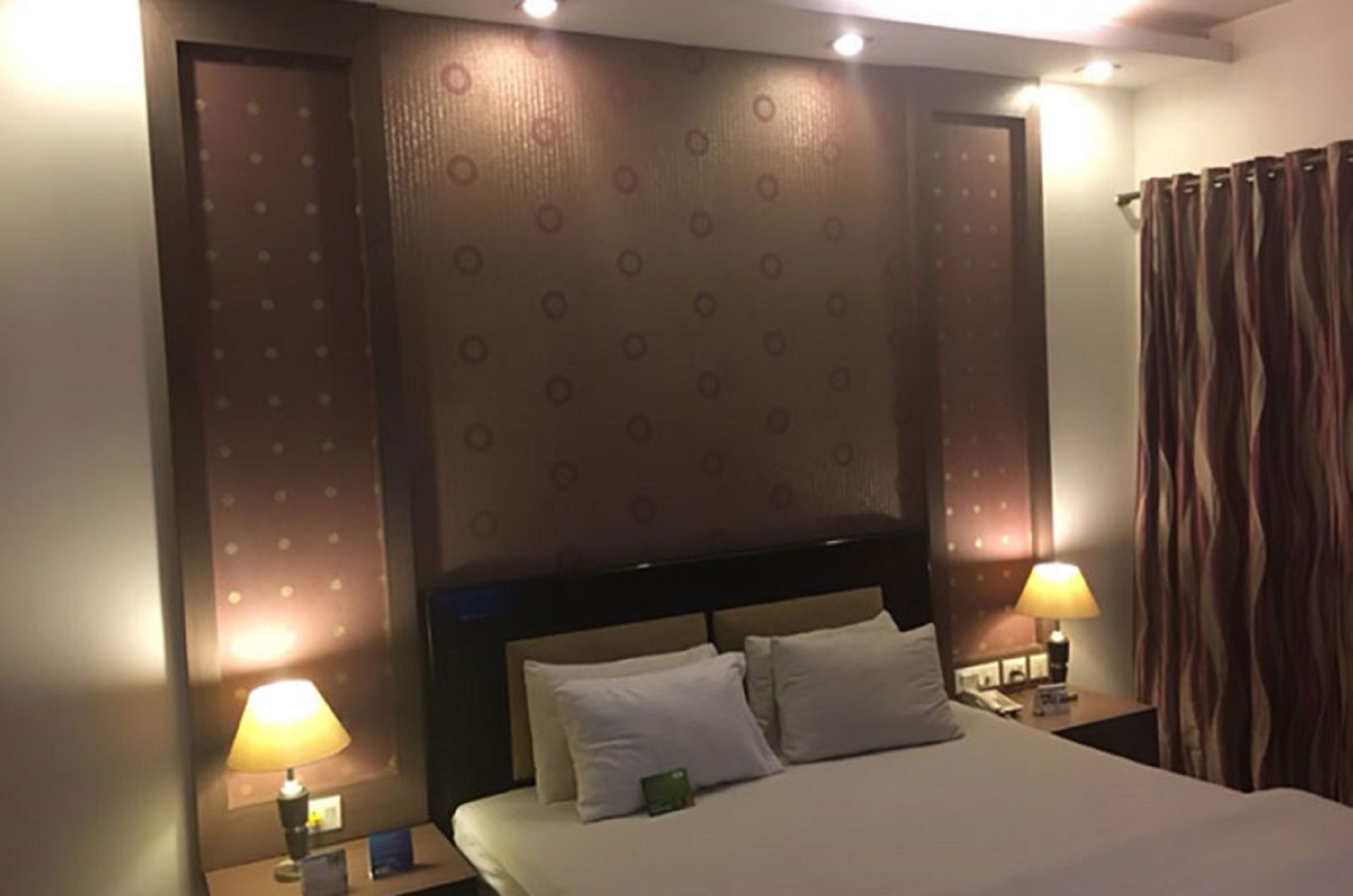 A hotel room with a large bed, two bedside tables with lamps, a headboard, and a patterned wall.