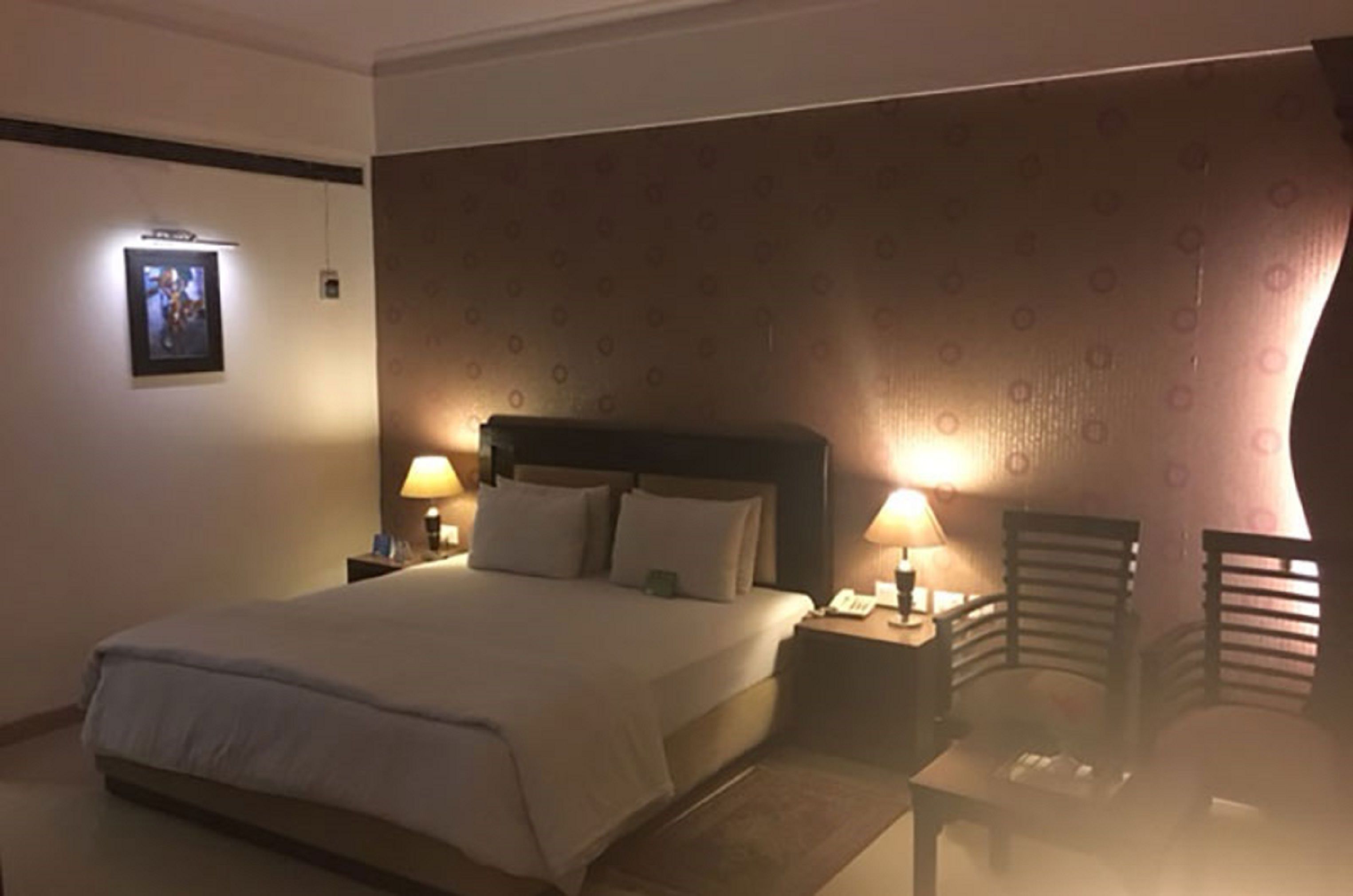 Una habitación de hotel con una cama grande, dos mesitas de noche con lámparas, un cabecero y una pared con diseño.