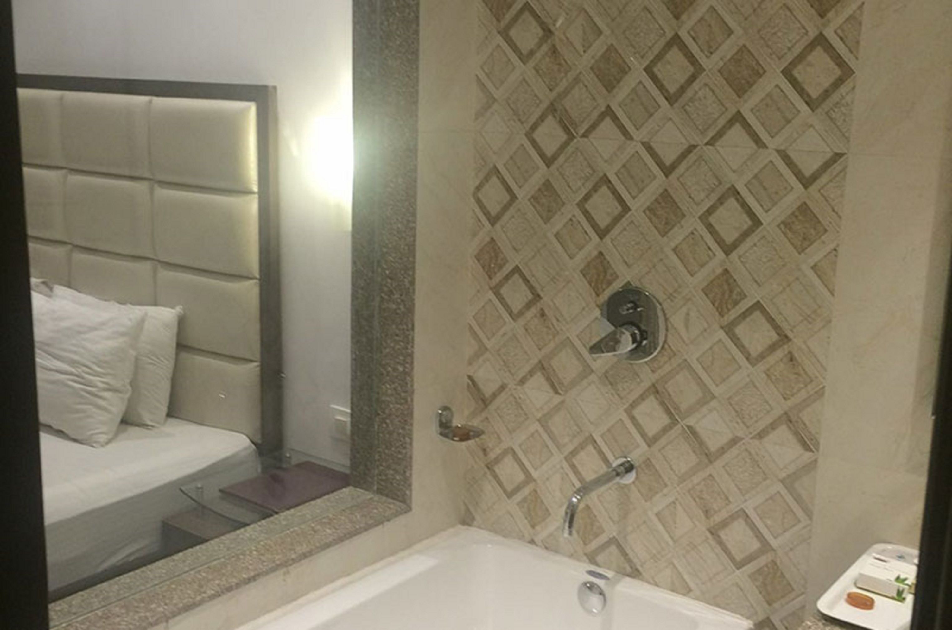 A bathroom with a bathtub, a mirror, and a patterned wall.