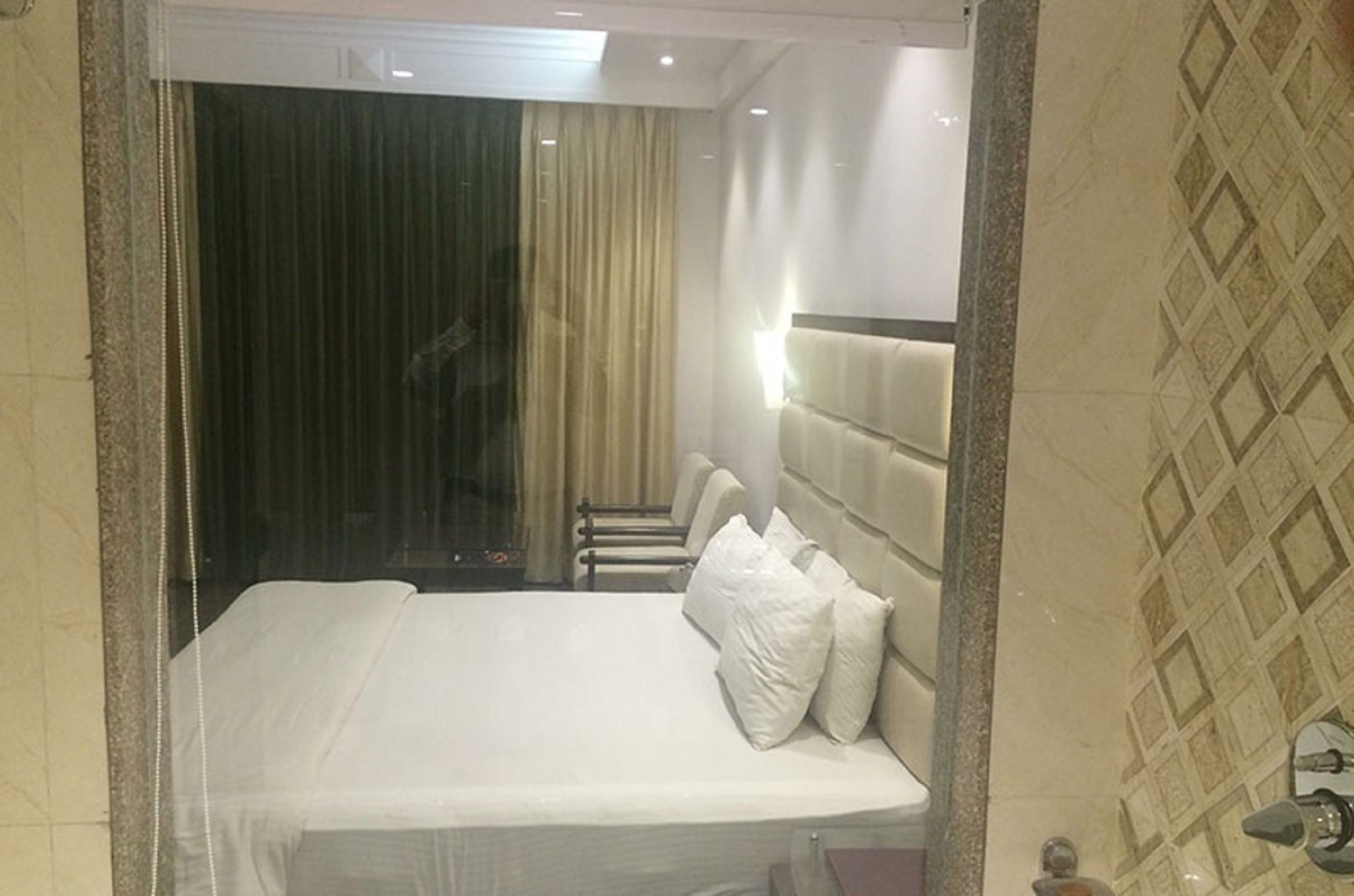 Ein Hotelzimmer mit Bett, Kopfteil, Spiegel und einem Fenster mit Vorhängen.