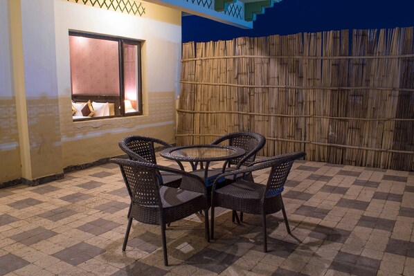 Una habitación con suelo a cuadros, una mesa redonda con sillas, una ventana con vistas y una pared de bambú.