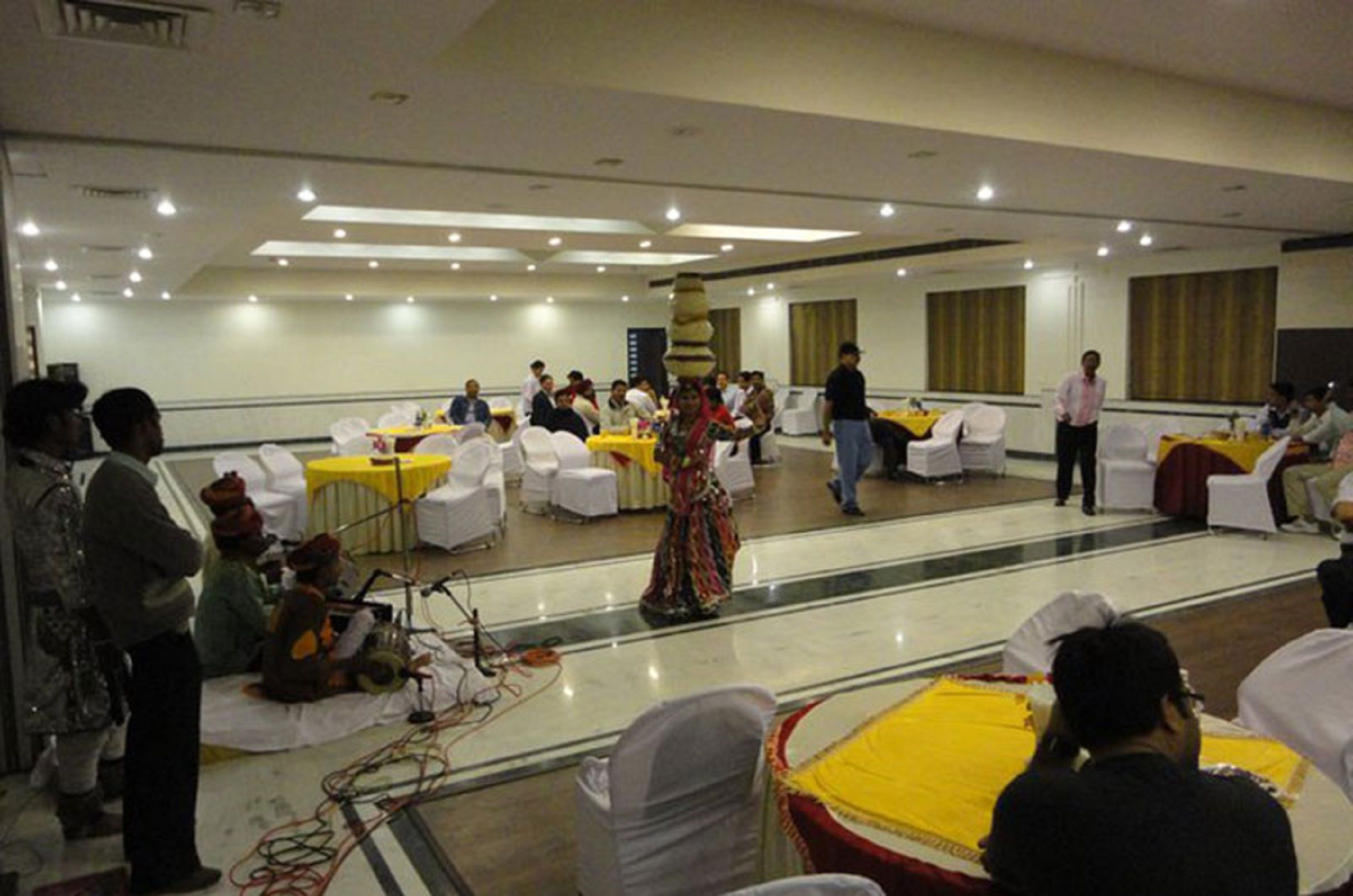 A banquet hall with round tables covered in white tablecloths, a stage with a performer, and attendees seated at tables.