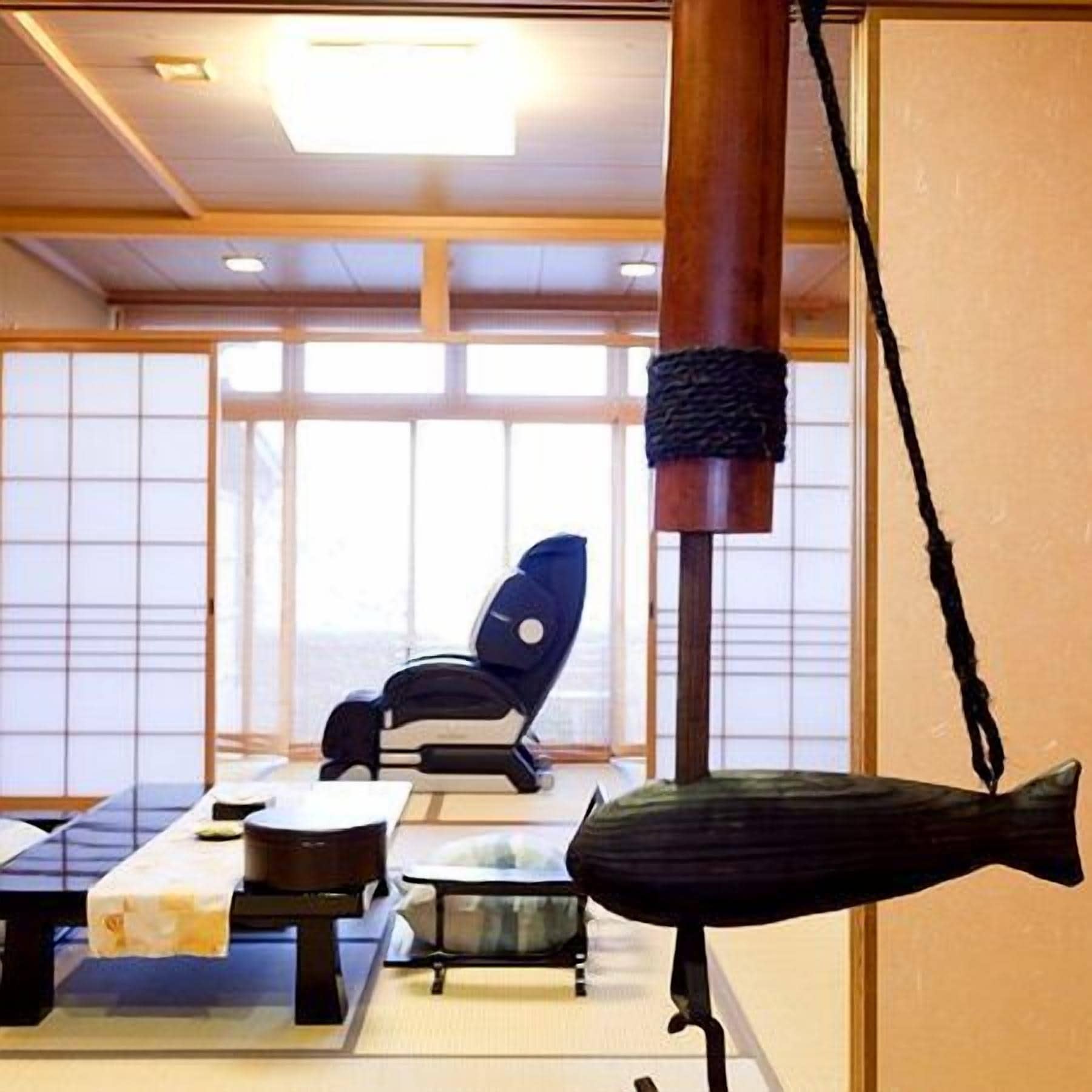 A traditional Japanese room with tatami flooring, a low table, a chair, and a large wooden pillar.