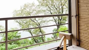 A hot spring bath with a wooden faucet, a view of trees through a window, and a bamboo blind.