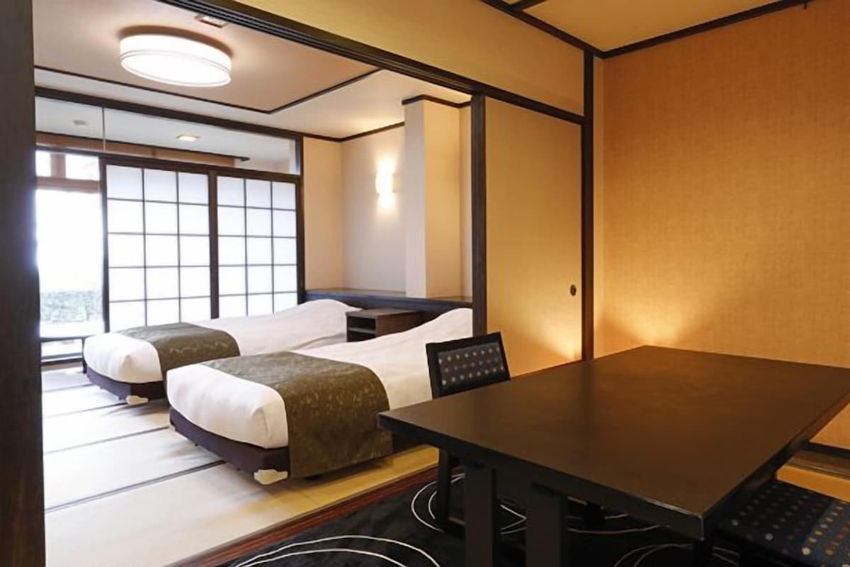 A hotel room with two beds, a dining table, and a view of the city.