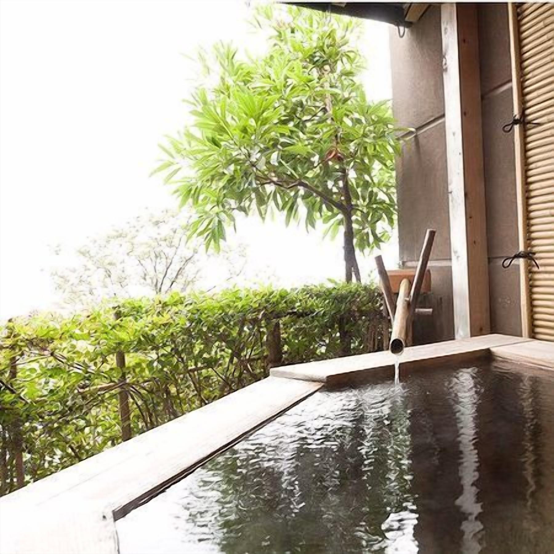 A pool with a wooden edge and a bamboo structure, surrounded by greenery.