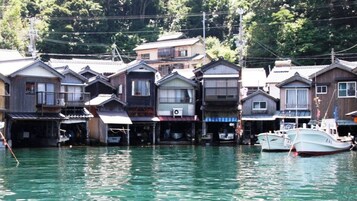 Fila de casas de madera tradicionales con un canal de agua delante, barcos amarrados y un promontorio boscoso al fondo.