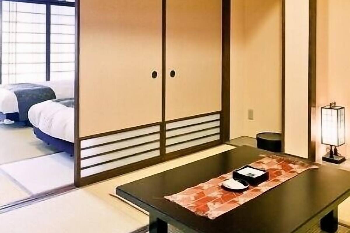 A traditional Japanese room with tatami flooring, a low table with a placemat, a bed, and sliding doors.