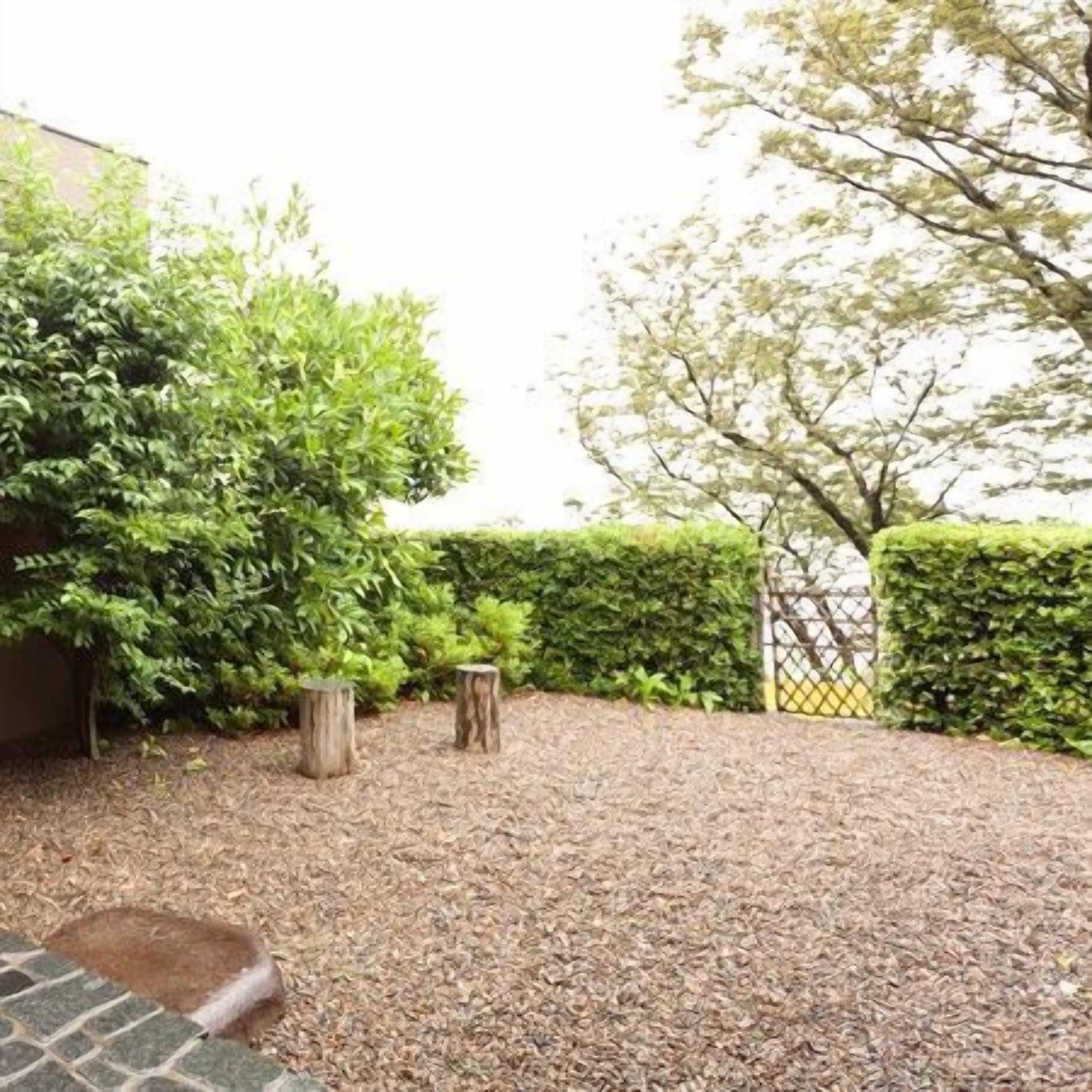 A gravel pathway leading to a building with a wooden fence and green hedges.