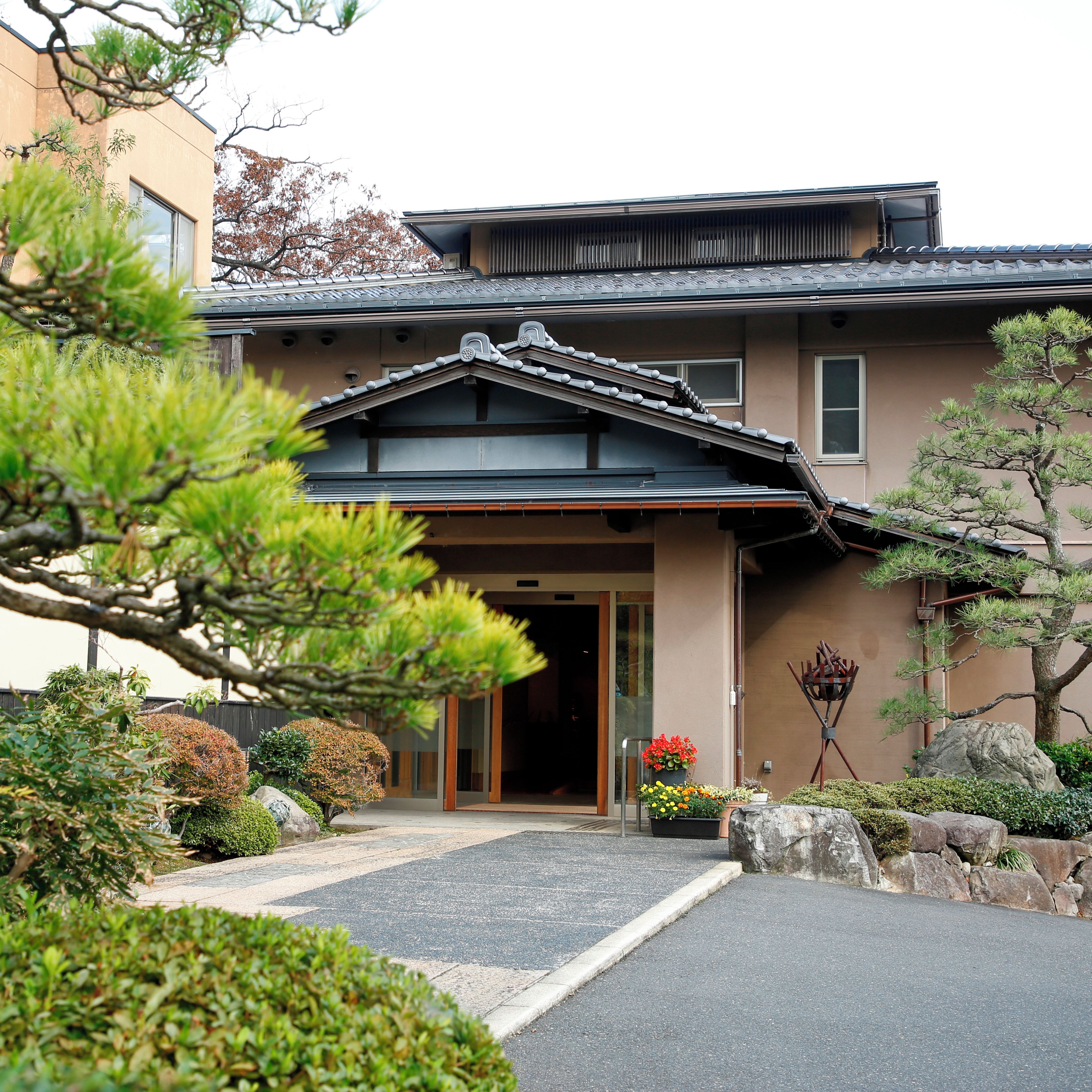 A traditional Japanese building with a tiled roof, a wooden entrance, and a well-maintained garden with rocks and plants.