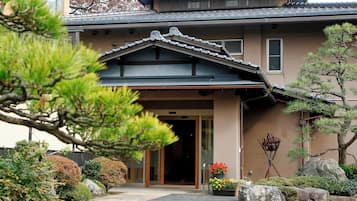 A traditional Japanese building with a tiled roof, a wooden entrance, and a well-maintained garden with rocks and plants.