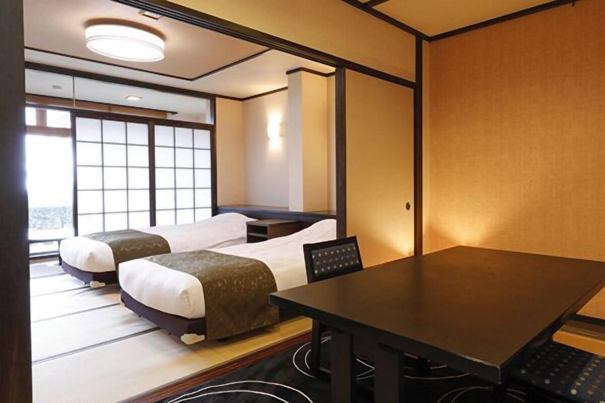 A hotel room with two beds, a dining table, and a view of the city.