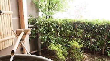 Un onsen japonés tradicional con un baño de piedra, estructuras de bambú y un jardín con valla de madera y follaje.