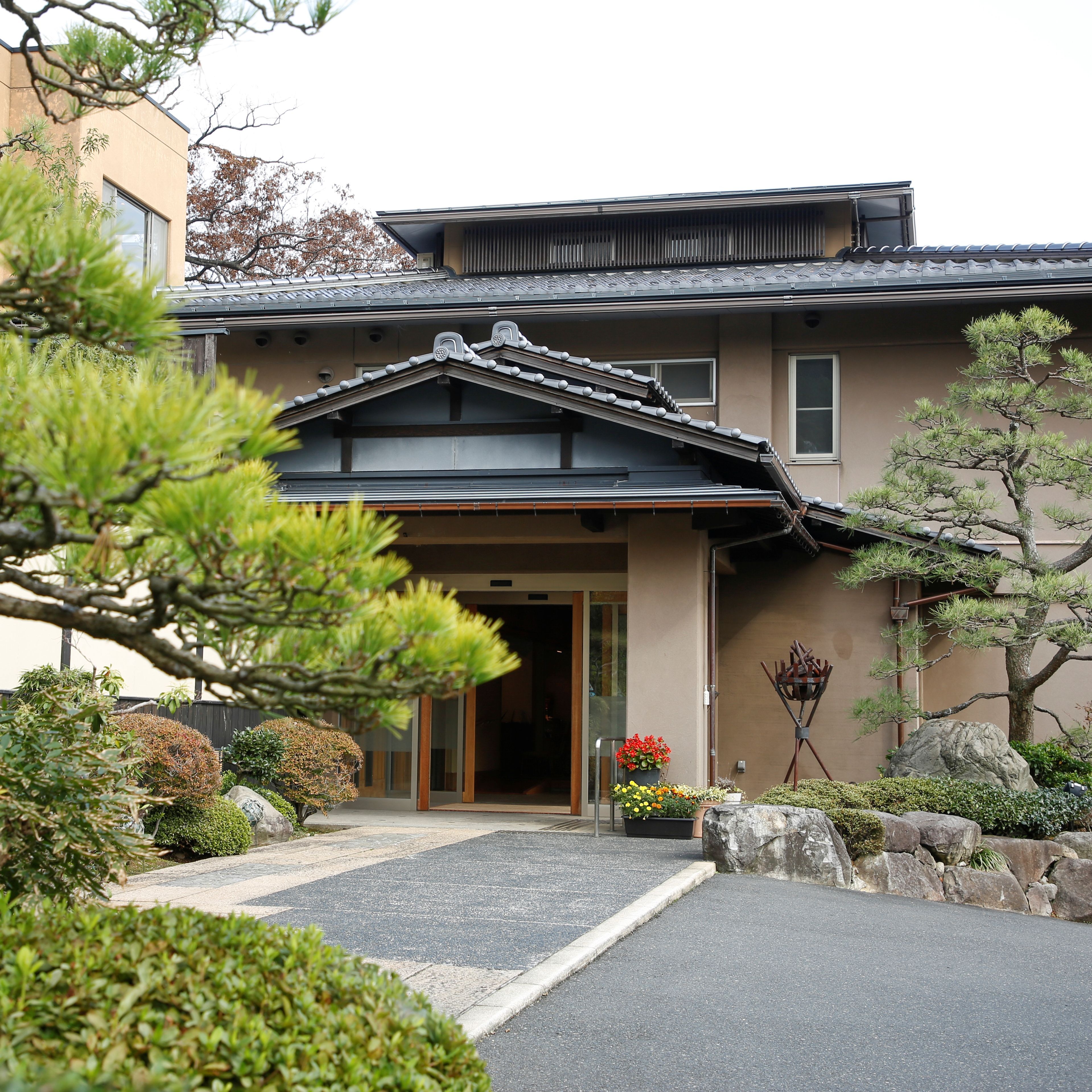 A traditional Japanese building with a tiled roof, a wooden entrance, and a garden with rocks and plants.