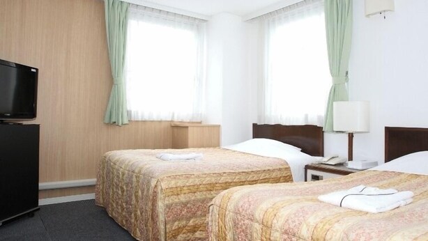 Habitación de hotel con dos camas, televisión, escritorio y lámpara.