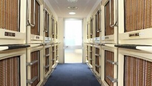 Un pasillo con hileras de habitaciones, cada una con un cartel con número, que conduce a una salida luminosa.