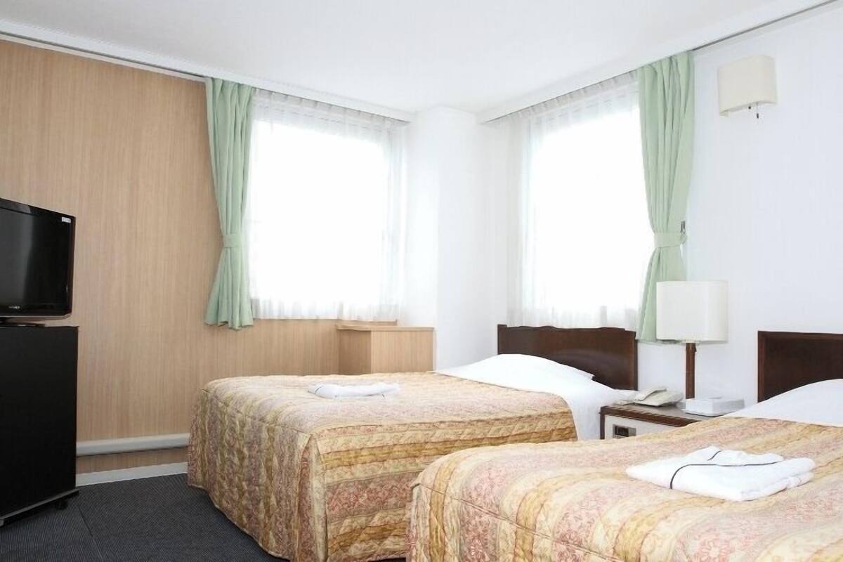 Une chambre d’hôtel avec deux lits, une télévision, un bureau et une lampe.