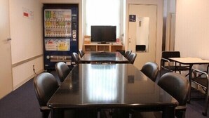 Una sala de conferencias con una larga mesa, sillas, un televisor, máquinas expendedoras y un ventanal.