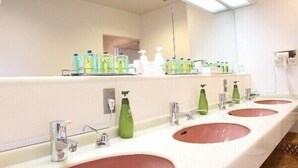 Un baño con tres lavamanos, cada uno con un espejo encima. Hay varias botellas de jabón y champú en la encimera.