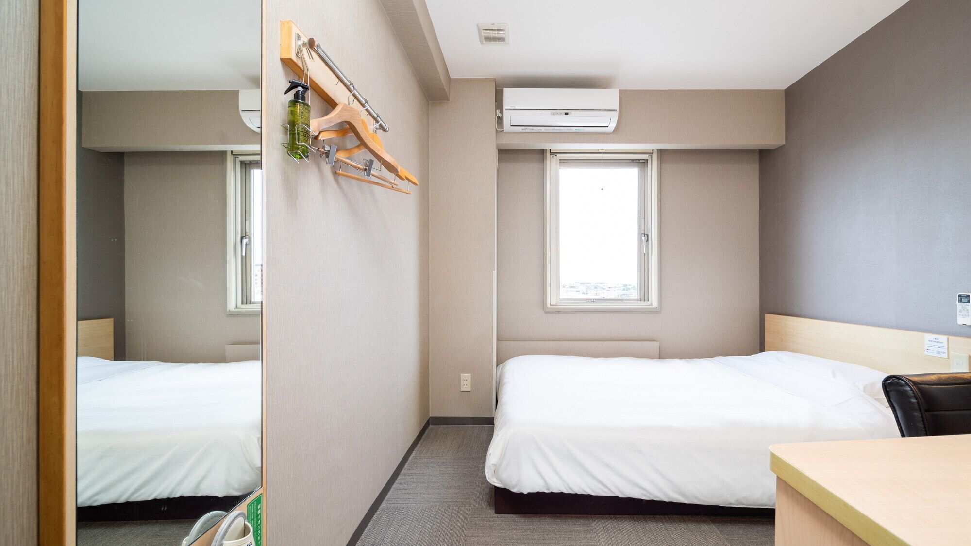 A hotel room with two beds, a desk, an air conditioning unit, and a window.