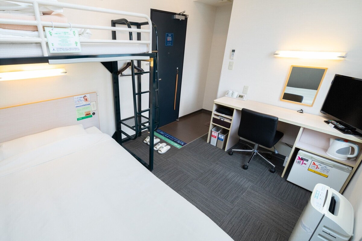 A hotel room with a bunk bed, desk, chair, computer, and a microwave.