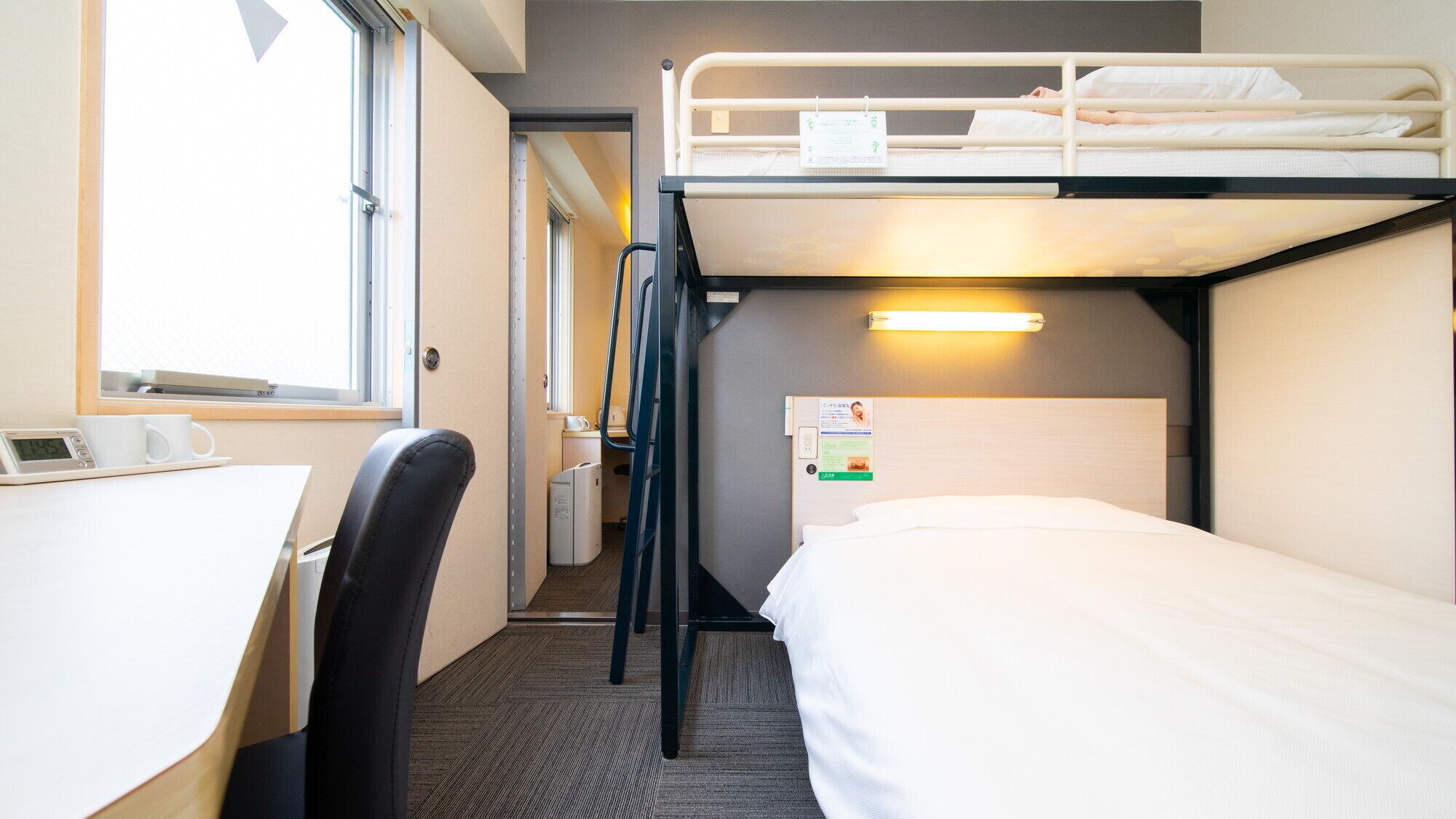 A bunk bed room with a desk, chair, and a window.