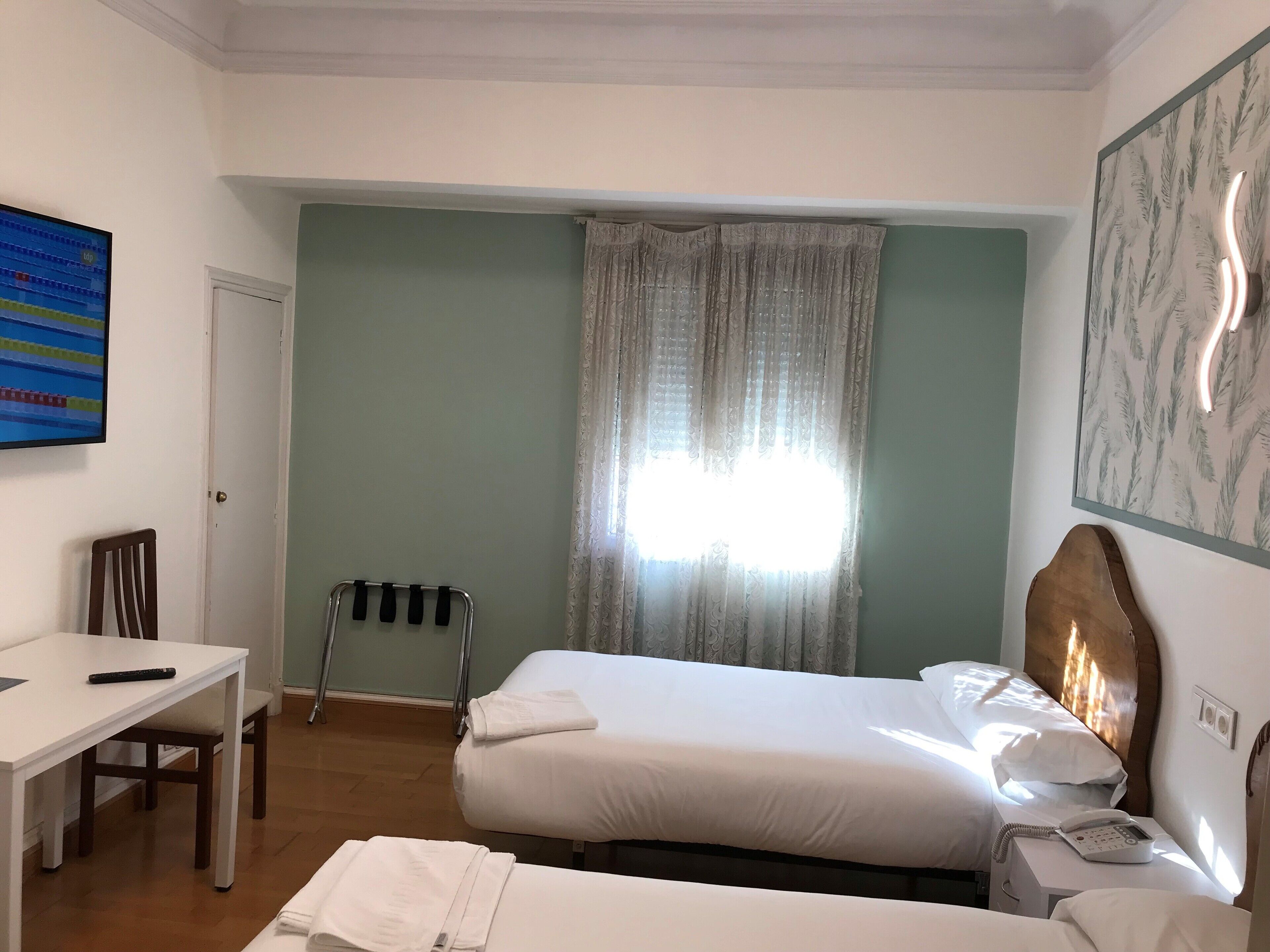 Habitación de hotel con dos camas, un escritorio, una silla, un teléfono y un cuadro en la pared.