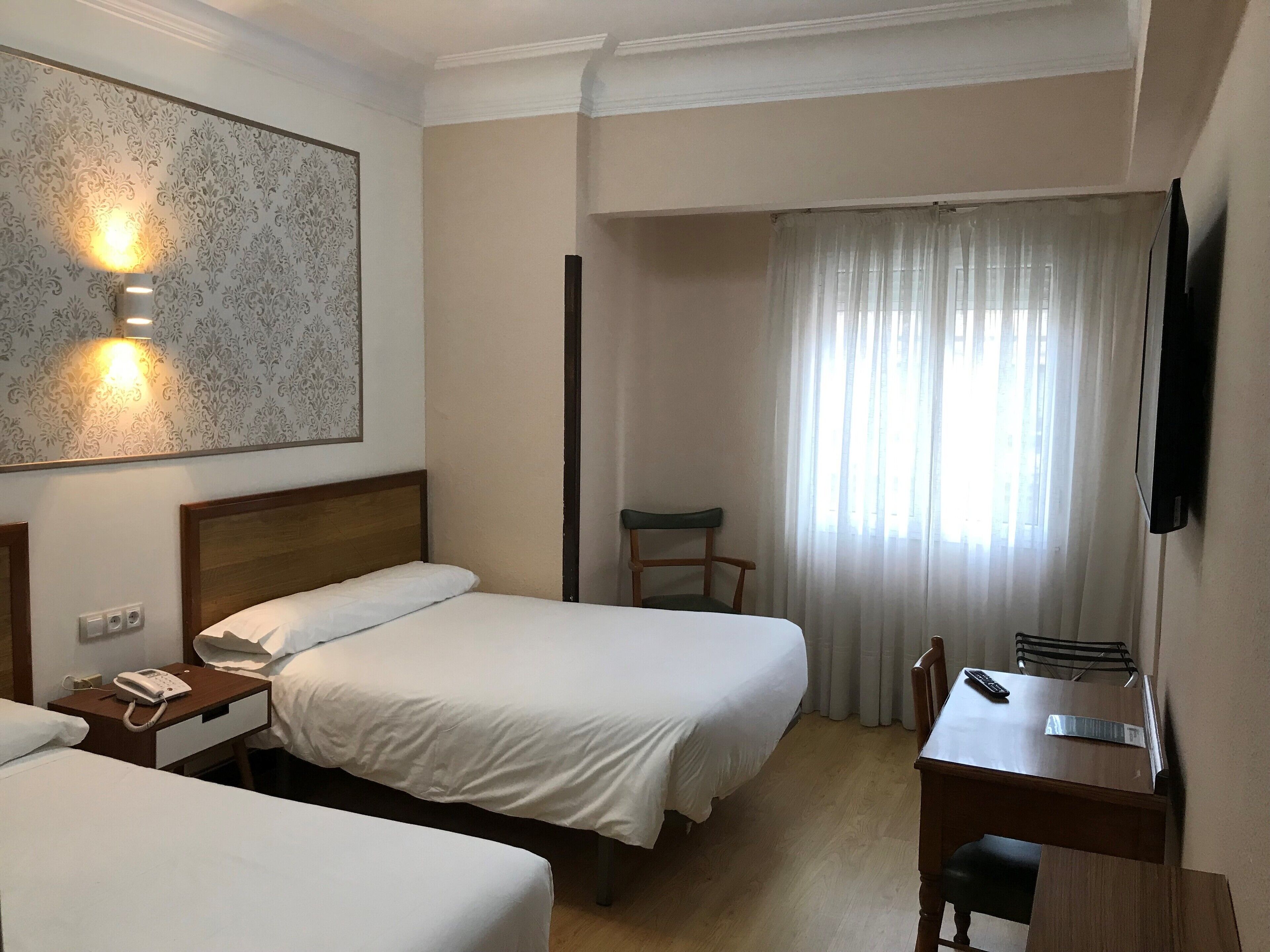 Habitación de hotel con dos camas, un escritorio con silla, televisión y teléfono.