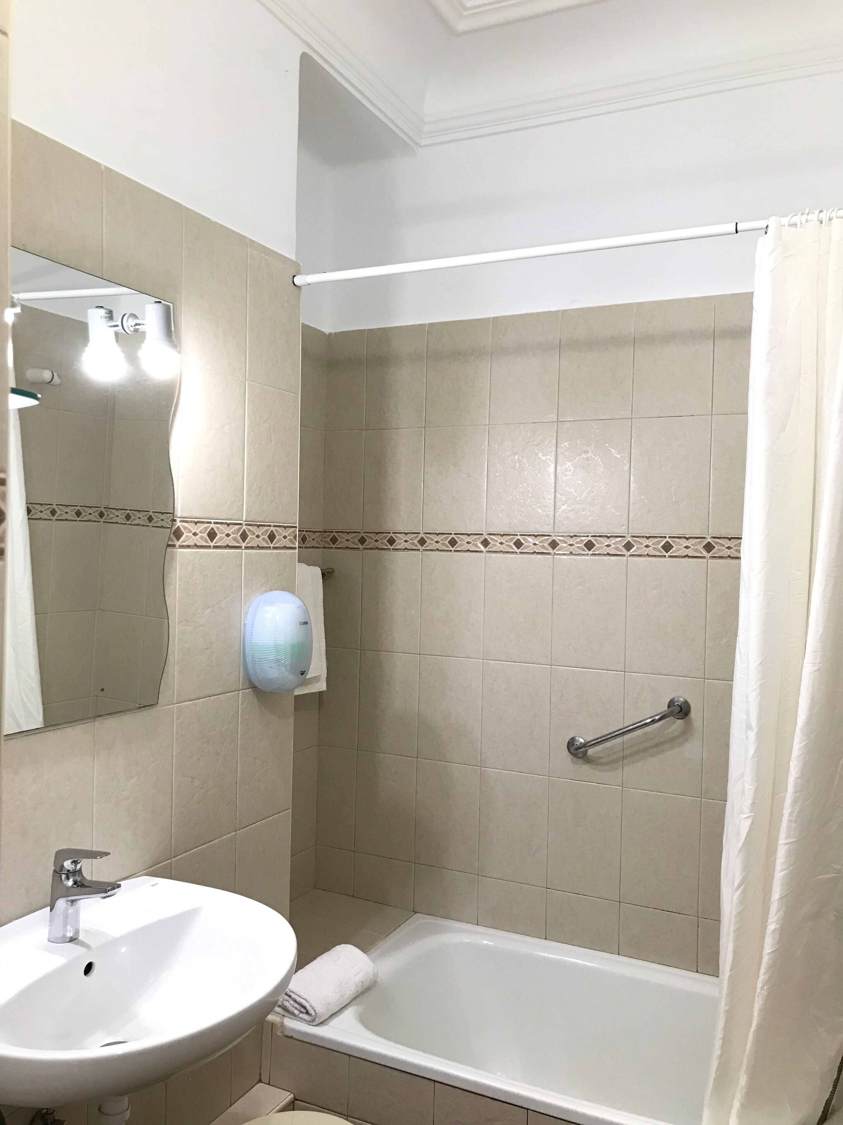 A bathroom with a sink, mirror, towel rack, shower curtain, and a hand dryer.