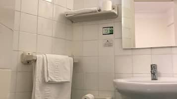 Un baño con azulejos blancos, inodoro, lavabo, toallero y dispensador de papel higiénico.